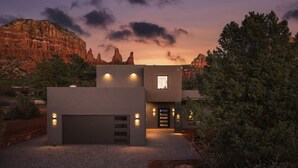 Una casa moderna de dos pisos con garaje, rodeada de árboles y montañas.