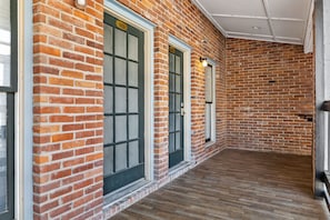 Un couloir aux murs de briques et aux grandes fenêtres, qui mène à une pièce dotée d’un plancher en bois.