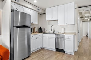 Une cuisine moderne avec des meubles blancs, des appareils en acier inoxydable et un plancher en bois.