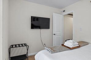 Ein Hotelzimmer mit einem Bett, einem an der Wand befestigten Fernseher, einer Tür und einem kleinen Tisch mit Handtüchern.