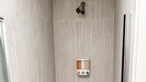 A shower with a control panel, a handheld showerhead, and a glass door.