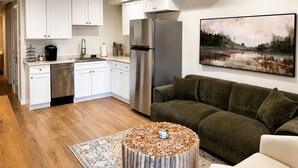 A modern kitchen with white cabinets, a stainless steel refrigerator, and a dining area with a wooden table and a patterned rug.