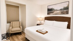 A hotel room with a bed, a chair, a lamp, and a painting on the wall.