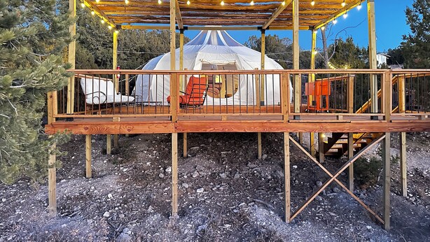 A yurt with a wooden deck and seating area, surrounded by trees.