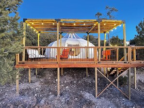 Una yurta con terraza de madera y zona de estar, rodeada de árboles.