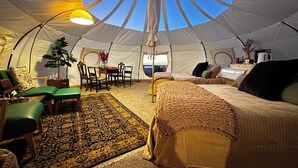 A tent with a central table, chairs, a bed, and a view of the sky through the ceiling.