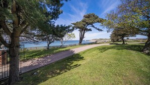 A pathway leading to a scenic view of the sea, surrounded by trees and a grassy area. - Holmes House - Sleeps 20 -Swimming pool -Sea Views (Colwell Bay)