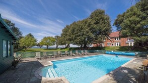 A rectangular swimming pool with a wooden deck and lounge chairs, surrounded by a wooden fence and trees, with a view of a building in the background. - Holmes House - Sleeps 20 -Swimming pool -Sea Views (Colwell Bay)