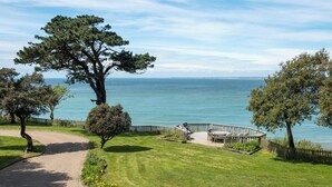 A pathway leading to a deck with outdoor furniture overlooking a body of water. - Holmes House - Sleeps 20 -Swimming pool -Sea Views (Colwell Bay)