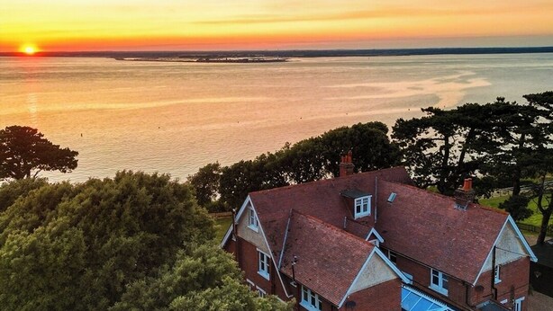 A house with a large bay window and a conservatory, overlooking a body of water during sunset. - Holmes House - Sleeps 20 -Swimming pool -Sea Views (Colwell Bay)