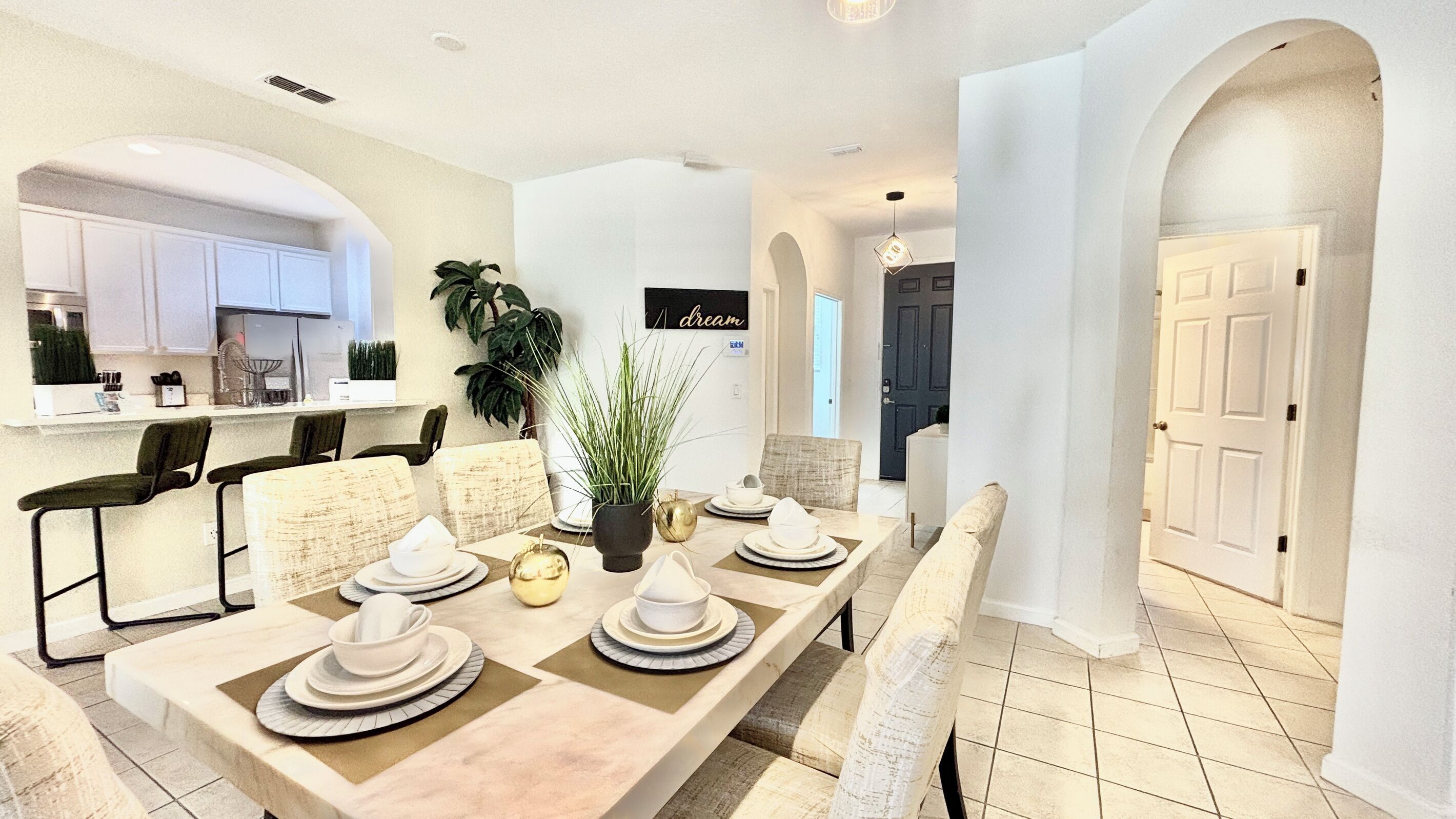 A modern dining area with a long table set for six, surrounded by chairs, and a kitchen area with white cabinets and a countertop.