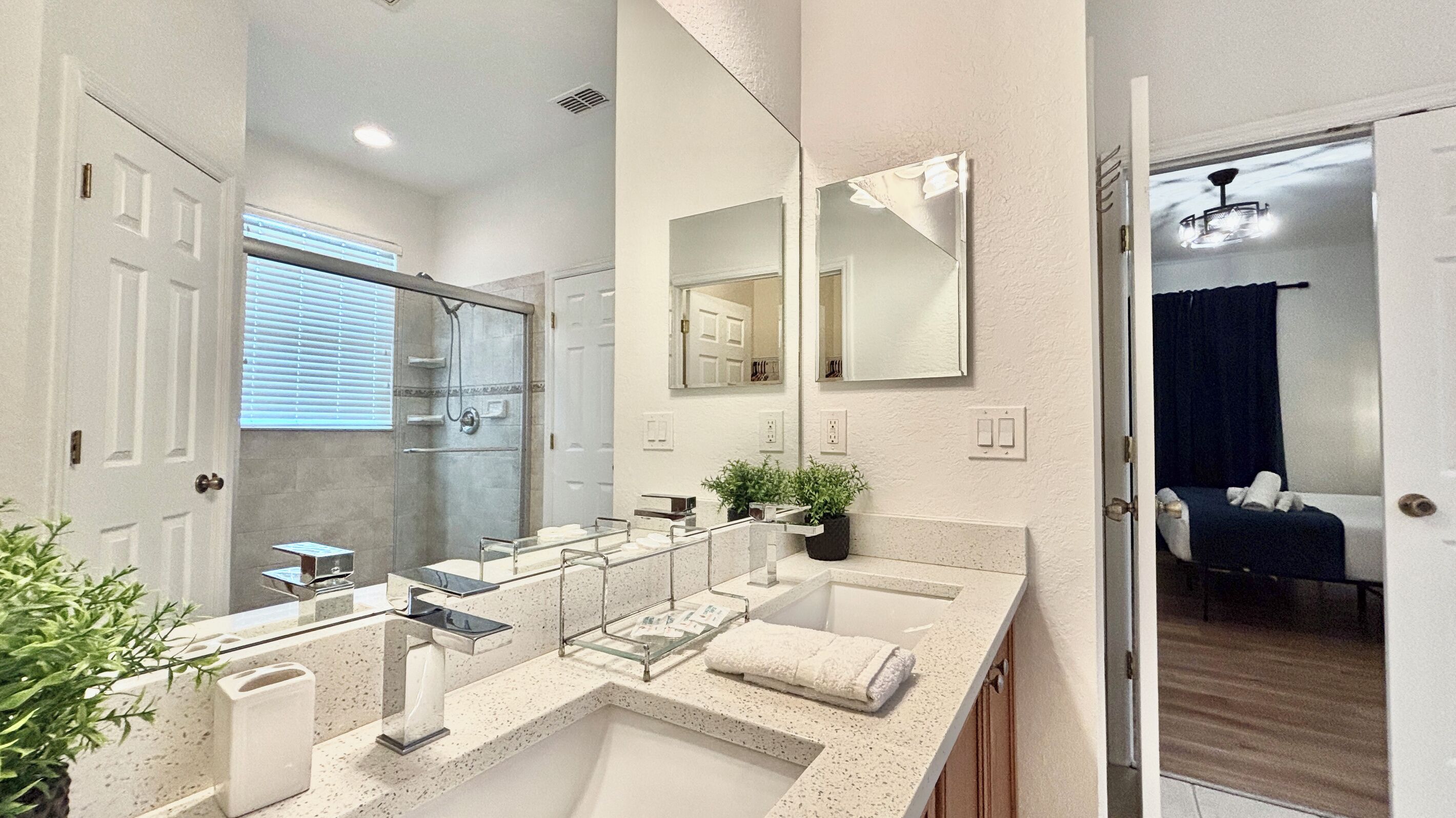 Un baño moderno con un espejo grande, una ducha y un tocador con lavabo y toallero.