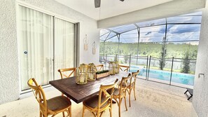 A dining area with a table and chairs, a view of a swimming pool, and a glass door leading outside. - 2632 Remodeled Getaway -heart of Disney (Kissimmee)