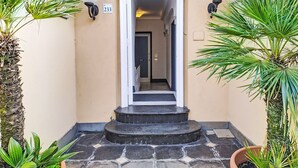 A building entrance with a stone staircase, a door with a number plate, and two wall-mounted light fixtures. - Laccadiva by Interhome (Zoagli)