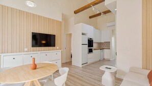 Una cocina moderna con armarios blancos, horno integrado y microondas. Hay una zona de comedor con una mesa redonda y sillas blancas.