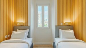 Habitación de hotel con dos camas, paredes de paneles de madera, una ventana y vistas a edificios.