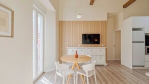 Una cocina moderna con un panel de madera en la pared, un televisor montado sobre la encimera y una zona de comedor con una mesa redonda y sillas blancas.