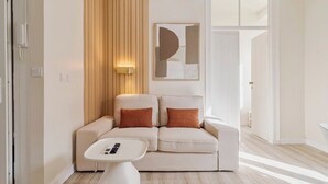 Un salón moderno con un sofá beige, dos cojines marrones, una mesa de centro blanca con un control remoto, una pared de acento de madera y un cuadro abstracto grande.