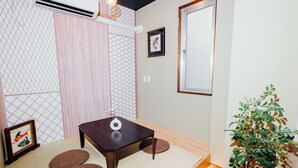 Ein Zimmer mit Tatami-Matten, einem dunklen Holztisch, einer kleinen Pflanze und einem gerahmten Bild an der Wand.