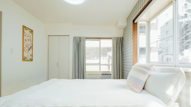 Ein Hotelzimmer mit einem großen Bett, einem Kleiderschrank, einem Fenster mit Vorhängen und einem an der Wand befestigten Kunstwerk.