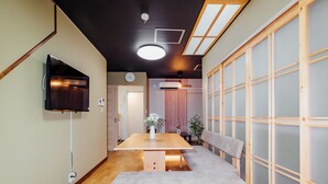Ein modernes Interieur mit einem Holztisch, einer Sitzbank, einem an der Wand montierten Fernseher und einem verschiebbaren Shoji-Bildschirm.