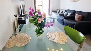 Een moderne woonkamer met een glazen eettafel, een zwarte bank en een groene fauteuil.
