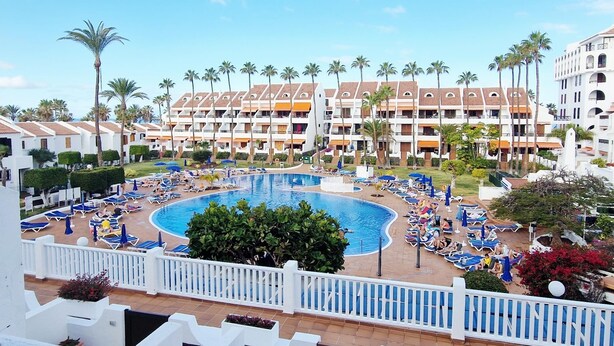 Een resort met een centraal gelegen zwembad, omringd door ligbedden en palmbomen.
