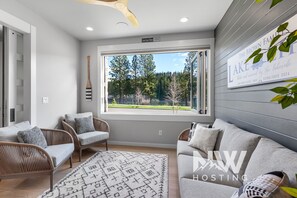 A modern living room with a large window, wicker furniture, and a decorative rug. - Luxury River-View Exec Stay – 90+ Days (Coeur D Alene)