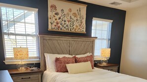 Une chambre à coucher avec un lit en bois, deux lampes de chevet, une table de nuit et une grande œuvre d’art florale au-dessus du lit.