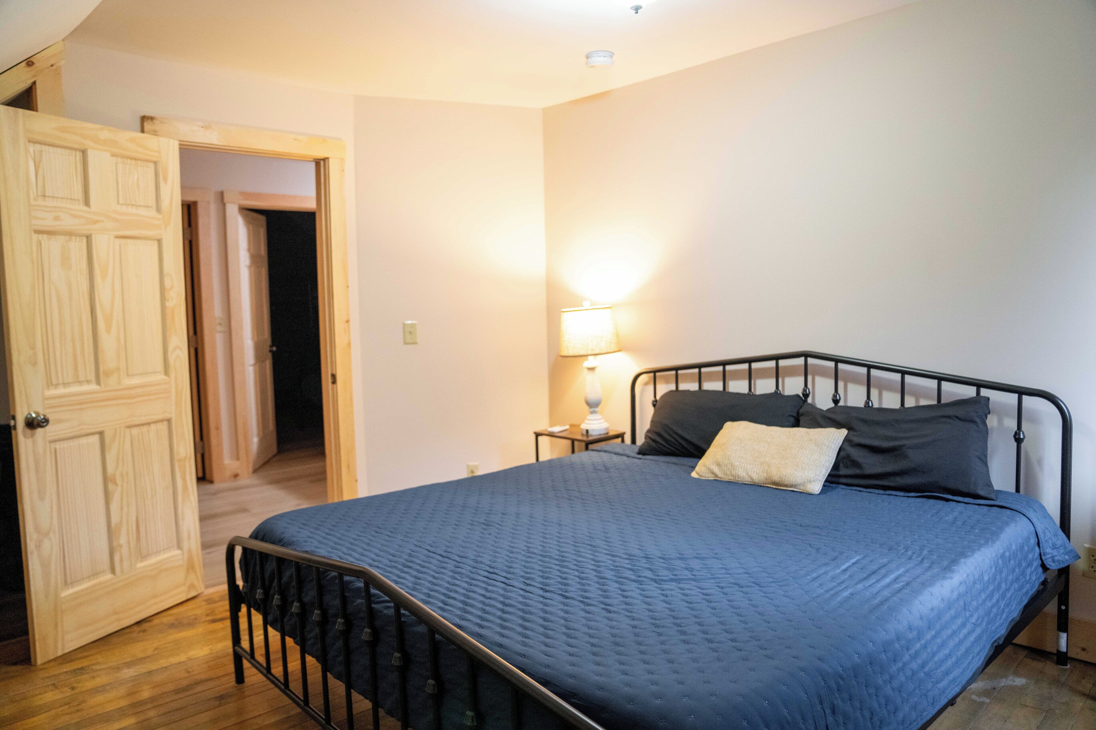 A bedroom with a bed, a nightstand, a lamp, and a wooden door.