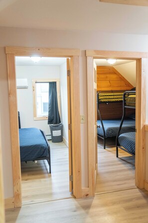 Una habitación con dos camas literas, una ventana con cortina, un cubo de basura y un ventilador de techo.