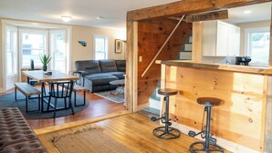 Una sala de estar moderna con una escalera de madera, un comedor y una zona de bar.