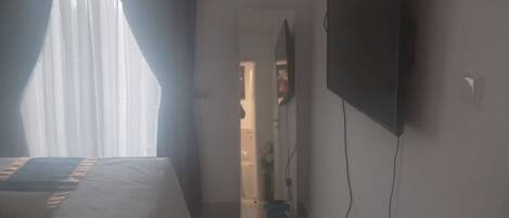 A hotel room with a bed, a TV mounted on the wall, and a door leading to a bathroom.