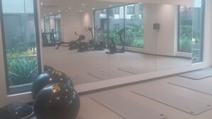 Moderni kuntosali, jossa on kuntoiluvälineitä, suuret ikkunat ja näkymä vehreään maisemaan.