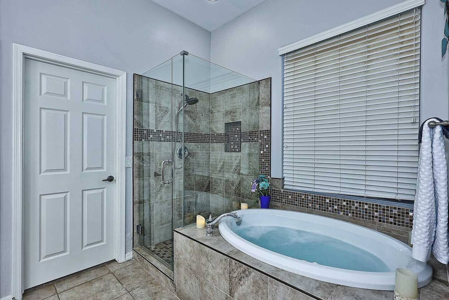 Un baño con ducha de vidrio, ba ñera y ventana con persianas.