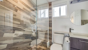 Een moderne badkamer met een douchecabine van glas, een toilet, een wastafel en een spiegel.