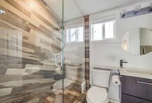 Ein modernes Badezimmer mit Duschkabine aus Glas, Toilette, Waschbecken und Spiegel.