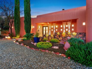 A modern building with a red facade, a well-lit entrance, and a landscaped garden with various plants and a gravel path. - Luxury Tigris House • Hot Tub • King Suites • Near Trails (Sedona)