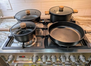 A kitchen with four black pots on a stove, a frying pan on the right burner, and a digital clock displaying 10:07. - Luxury Tigris House • Hot Tub • King Suites • Near Trails (Sedona)