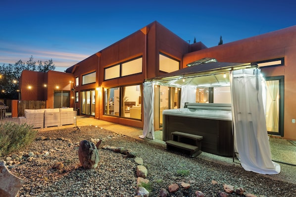 A modern house with a patio area featuring a hot tub, outdoor seating, and a well-maintained garden. - Luxury Tigris House • Hot Tub • King Suites • Near Trails (Sedona)
