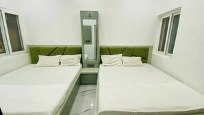Une petite chambre propre, avec deux lits simples, un miroir et une petite table.