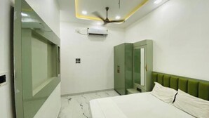 Une chambre à coucher comprenant un lit, une tête de lit recouverte d’un tissu vert, un ventilateur de plafond et un appareil de climatisation.
