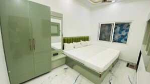 Une chambre à coucher comprenant un lit, une armoire, un miroir et une fenêtre ornée d’un motif géométrique.