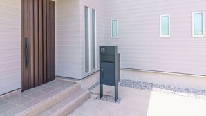 A modern building exterior with a wooden door, a mailbox, and a small set of steps leading to the entrance. - BURIKINA TERRACE (Nago)