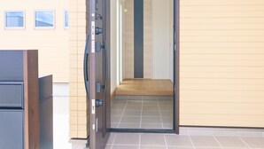 A hallway with a wooden door, a tiled floor, and a light-colored wall with three small windows. - BURIKINA TERRACE (Nago)