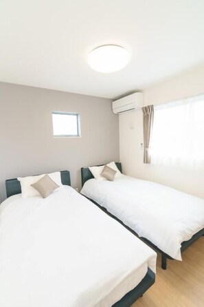 A room with two single beds, a small window, an air conditioning unit, and a curtain.