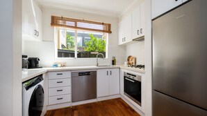 Een moderne keuken met witte kasten, roestvrijstalen apparatuur en een raam met uitzicht op groen.