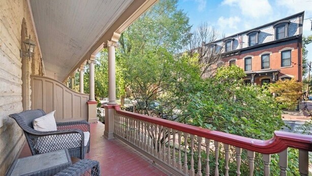 A covered porch with wicker furniture, a red railing, and a view of neighboring buildings. - "Friends" House/Mins to Stadiums/Free Parking/Hot Tub/Pets Welcomed (Pittsburgh)