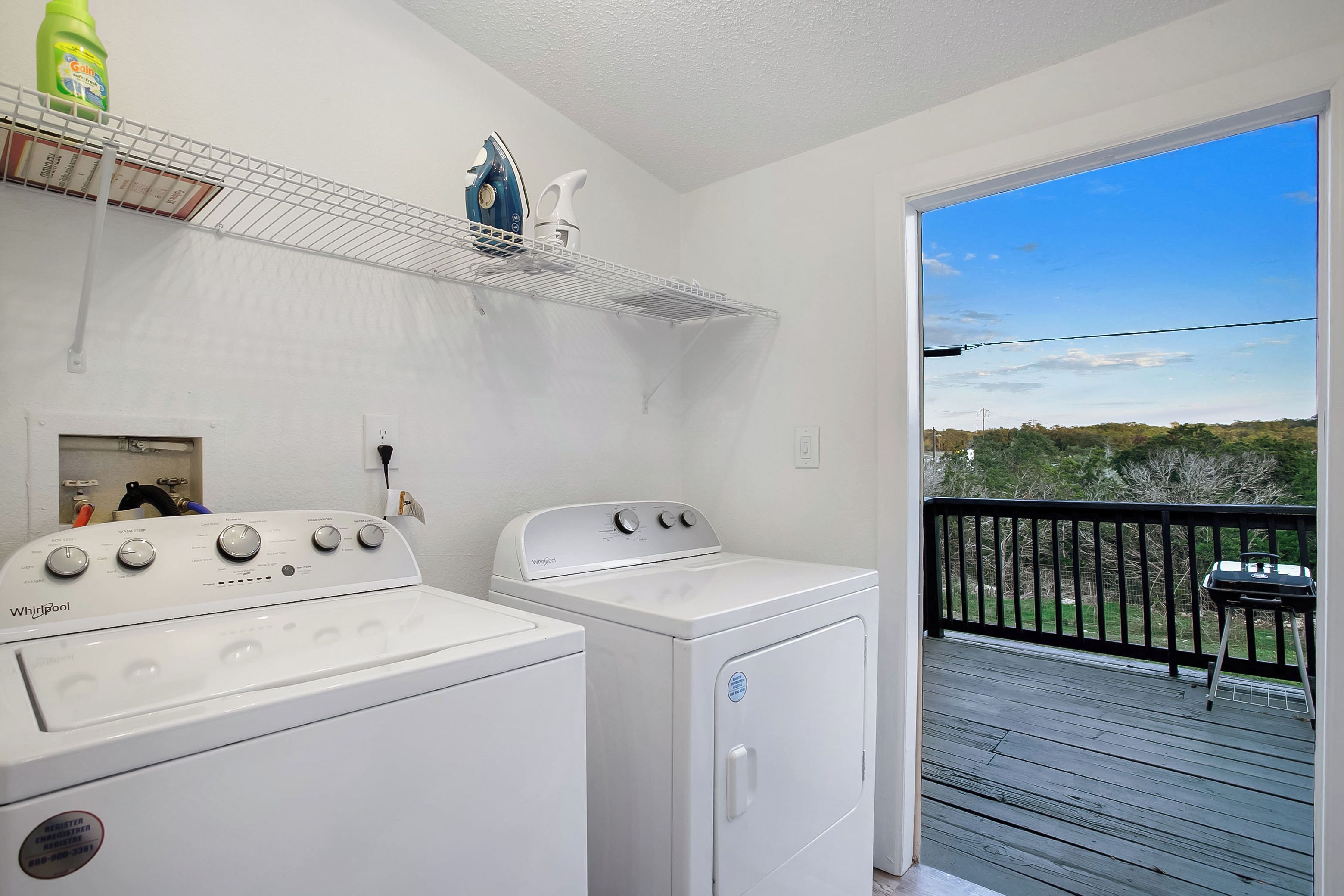 A laundry area with a washer and dryer, a shelf with cleaning supplies, and a balcony with a view of the outdoors.