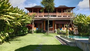 A two-story building with a balcony, surrounded by lush greenery and a swimming pool. - Rana Suite (Ubud)